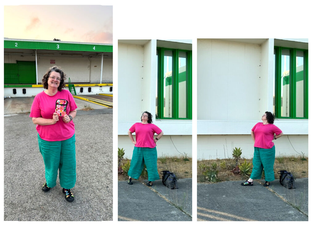 A woman in a hot pink blouse and blue-green trousers poses in front of a white building with green trim with a pen case that has all the same bright colors in it