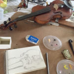 Violin on table with a drawing of it in progress, art supplies surround the paper